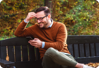 Un hombre mira su teléfono y sonríe en un banco del parque