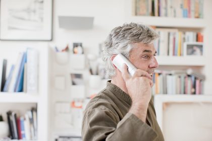 Un hombre con barba de mediana edad hablando por un teléfono inalámbrico.