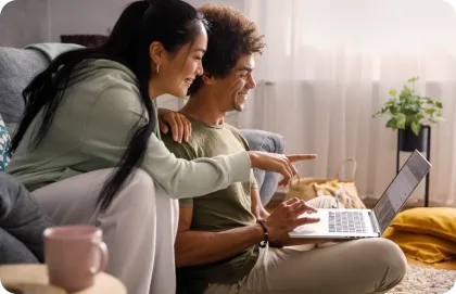 Una pareja sentada en un sofá trabajando juntos en una laptop.