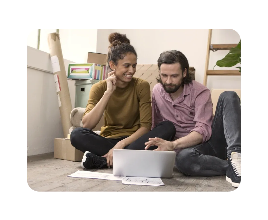 Pareja sentada en el suelo configurando su Internet Breezeline en la laptop, en su nuevo hogar.