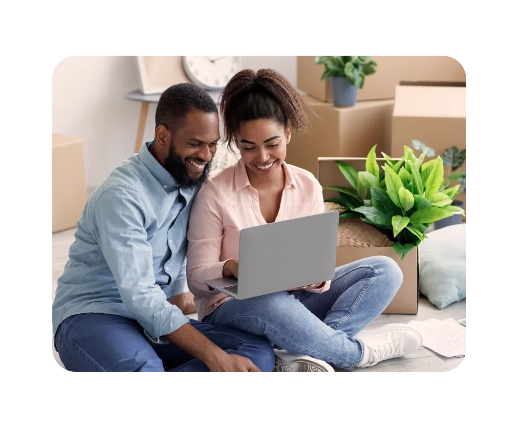 Pareja instalando Internet en casa con su laptop, rodeada de cajas de mudanza y plantas.