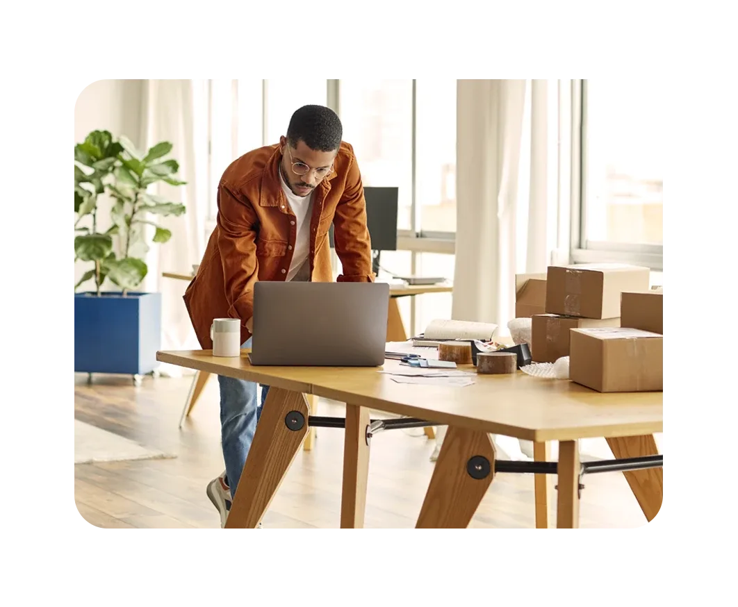 Hombre navegando por internet frente a una mesa con cajas de mudanza a su alrededor
