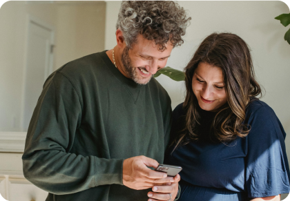 Un hombre y una mujer sonríen mientras miran un dispositivo móvil
