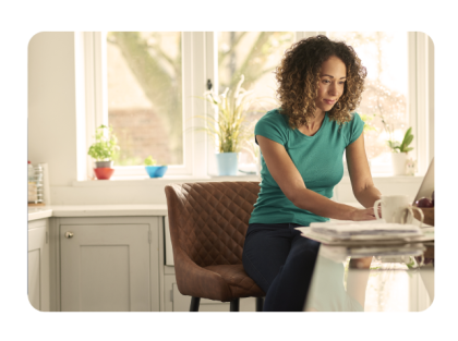Mujer sentada en una silla en la cocina con una laptop y una taza de café