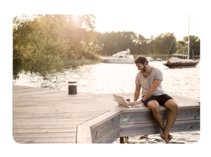 Hombre sentado en un muelle con una laptop junto al lago