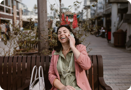 Una mujer sonríe mientras habla por teléfono en un banco al aire libre