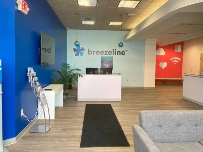 Interior de un centro comercial de varios niveles con tiendas, en donde aparece un kiosco de Breezeline.