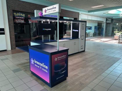 Un kiosco de servicio móvil, de TV y de Internet de Breezeline, de color azul y blanco, en el corredor de un centro comercial.