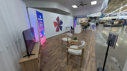 Una cabina promocional de Internet de Breezeline dentro de un Walmart, con un fondo de la marca, un letrero luminoso, una pantalla de TV y una pequeña área de estar.