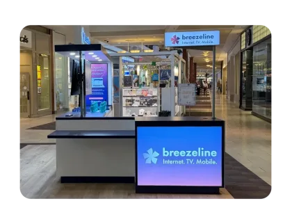 Interior of a multi-level shopping mall with storefronts, featuring a Breezeline kiosk.