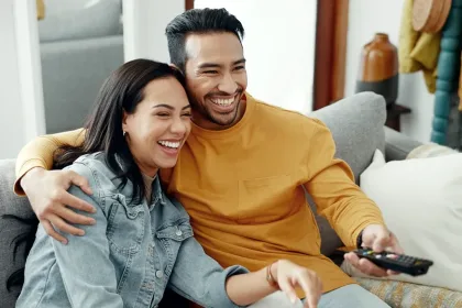 Una pareja sonriendo y mirando TV juntos en su sala de estar.