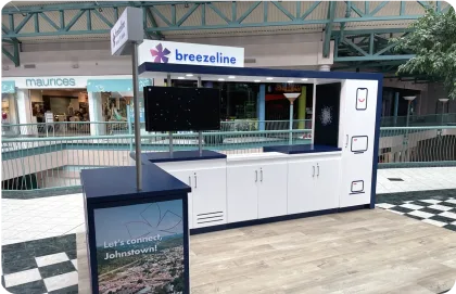 Interior de un centro comercial de varios niveles con tiendas, en donde aparece un kiosco de Breezeline.