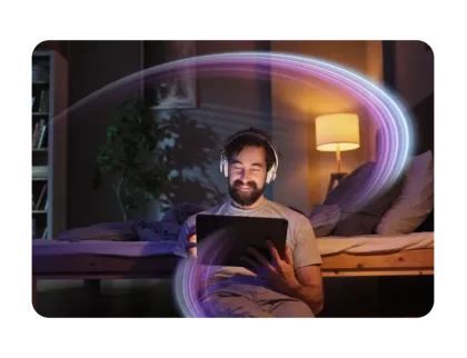 Smiling man in a dark bedroom wearing headphones and looking at a tablet, surrounded by a glowing colorful swoosh.