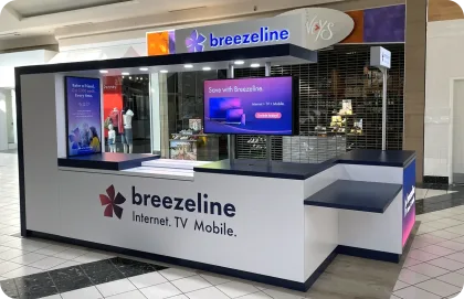 Interior de un centro comercial de varios niveles con tiendas, en donde aparece un kiosco de Breezeline.
