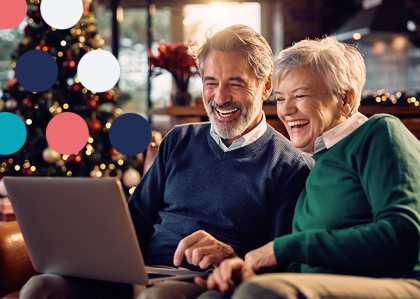Un hombre y dos mujeres reunidos alrededor de una laptop sonriendo y riendo con una decoración festiva de fondo