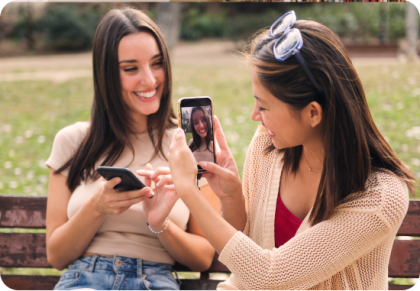 Dos mujeres sentadas en un banco del parque sonriendo y tomando fotos con sus teléfonos móviles