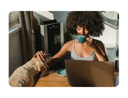 Mujer bebiendo sorbos de una taza en una mesa con una laptop mientras acaricia a un perro