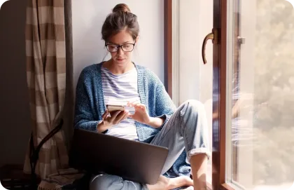 Una mujer sentada en el alféizar de la ventana y escribiendo en su laptop.