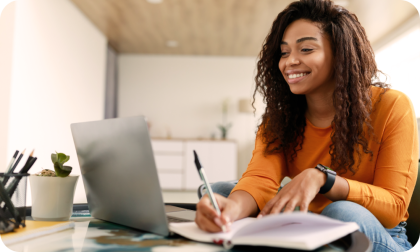 Woman with notebook and pen smiling beside laptop