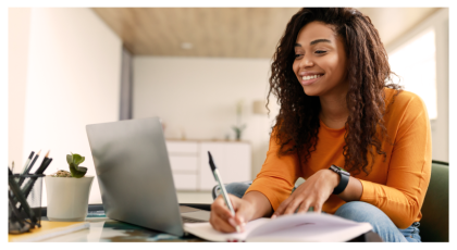 Estudiante sonriendo y escribiendo en un cuaderno al lado de una laptop